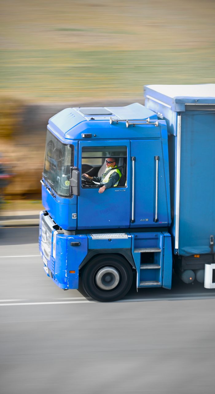 Services Dynamic panning shot capturing a blue truck in motion on a highway in daylight.